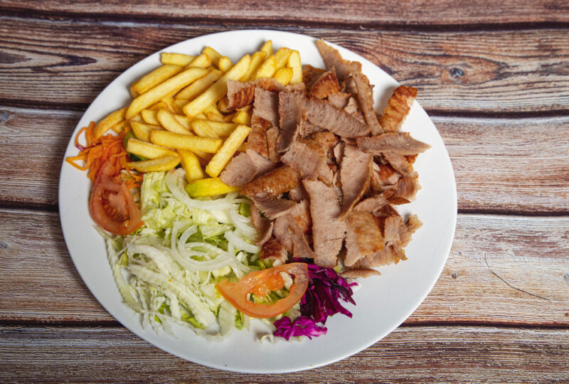 Beef doner on a plate with french fries and salad on wooden background.